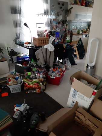 Unordentliche Küche mit vielen Kartons, Haushaltswaren und Verpackungen auf dem Boden.