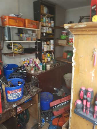 Unordentliche Werkstatt mit Regalen voller Werkzeug, Farbeimer, Schraubenziehern und Zubehör.