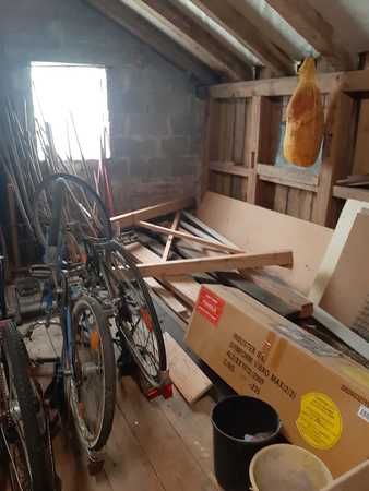Dachboden mit alten Fahrrädern, Holzlatten, Kartons und hängendem Schinken am Balken.