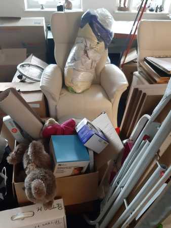 Ein vollgestellter Umzugsraum mit Kartons, Möbeln, Kuscheltieren und Umzugskisten.